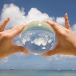 Saipan. One hands is holding a glass sphere and it projects the sky and the clouds at the beach.